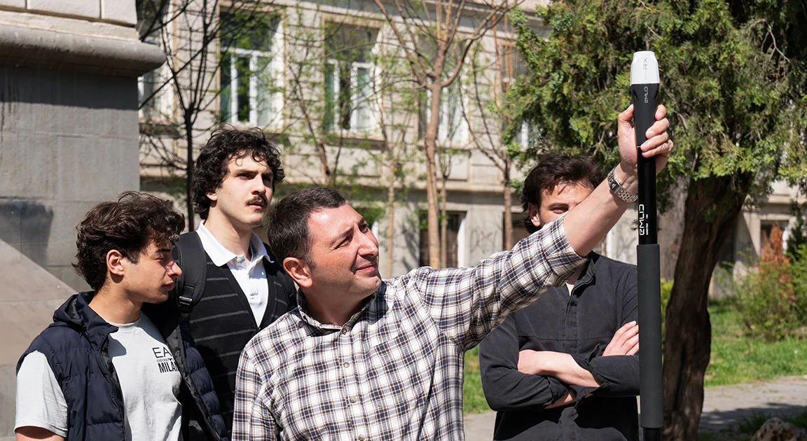 Students looking up at a GNSS rover pole held by an application engineer on campus